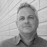 In black and white. A portrait of a man with hair. He is wearing a checkered shirt.