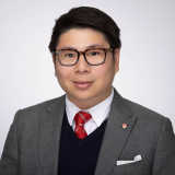 Thomas Nguyen wearing a grey blazer, navy sweater, white shirt and red tie