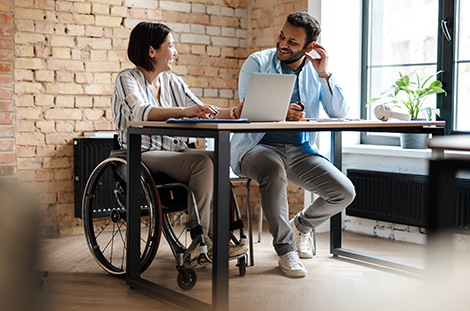 Female in wheelchair and male working at a desk with a laptop