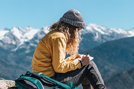 Female student writing in book on top of mountain