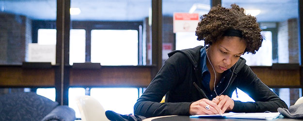 Image of female-presenting Black student working at a desk in a library
