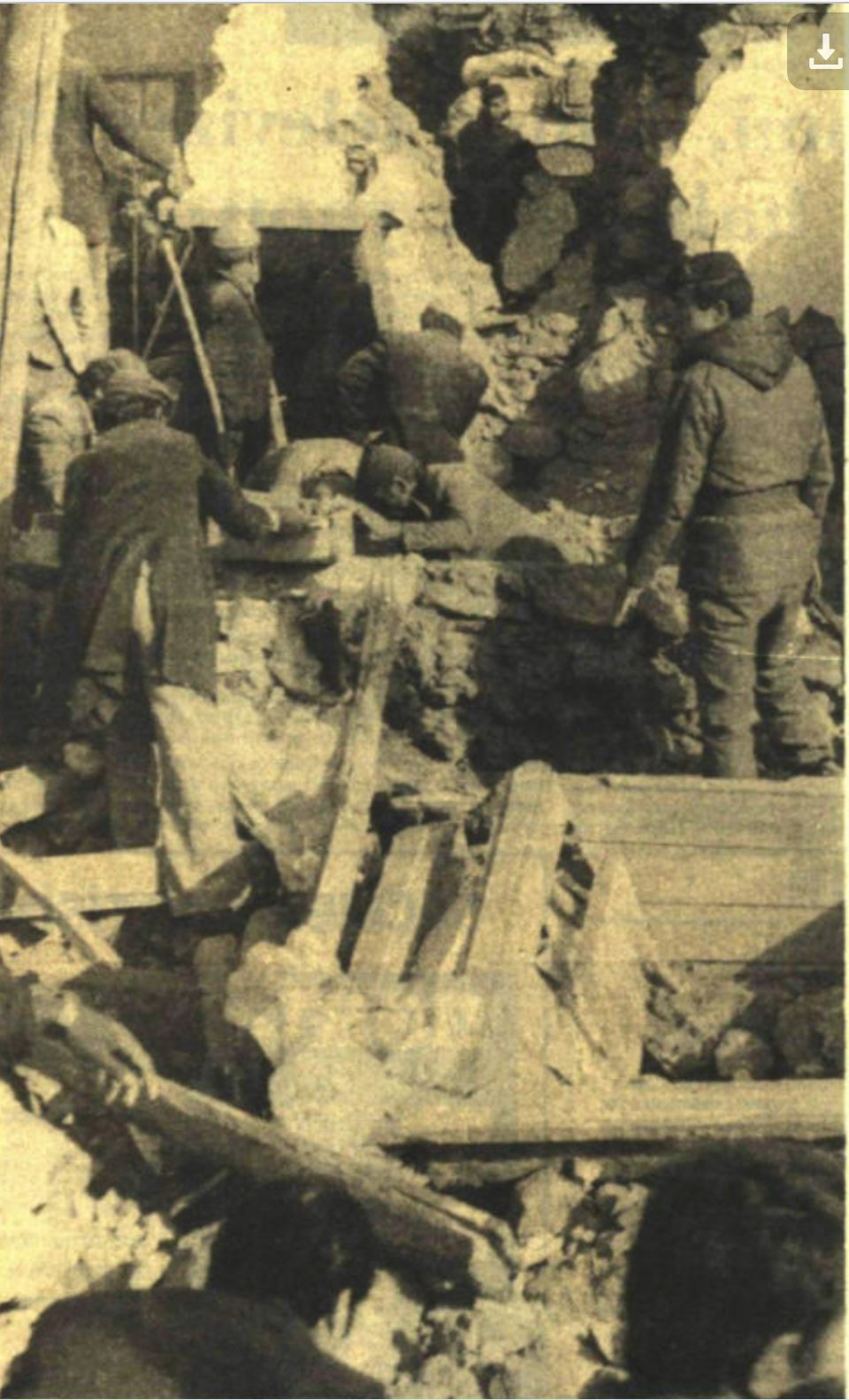 The photograph shows a group of people searching a ruined site of collapsed buildings due to the earthquake.