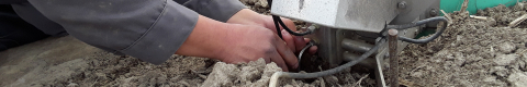Close up of hands working on device on dirt