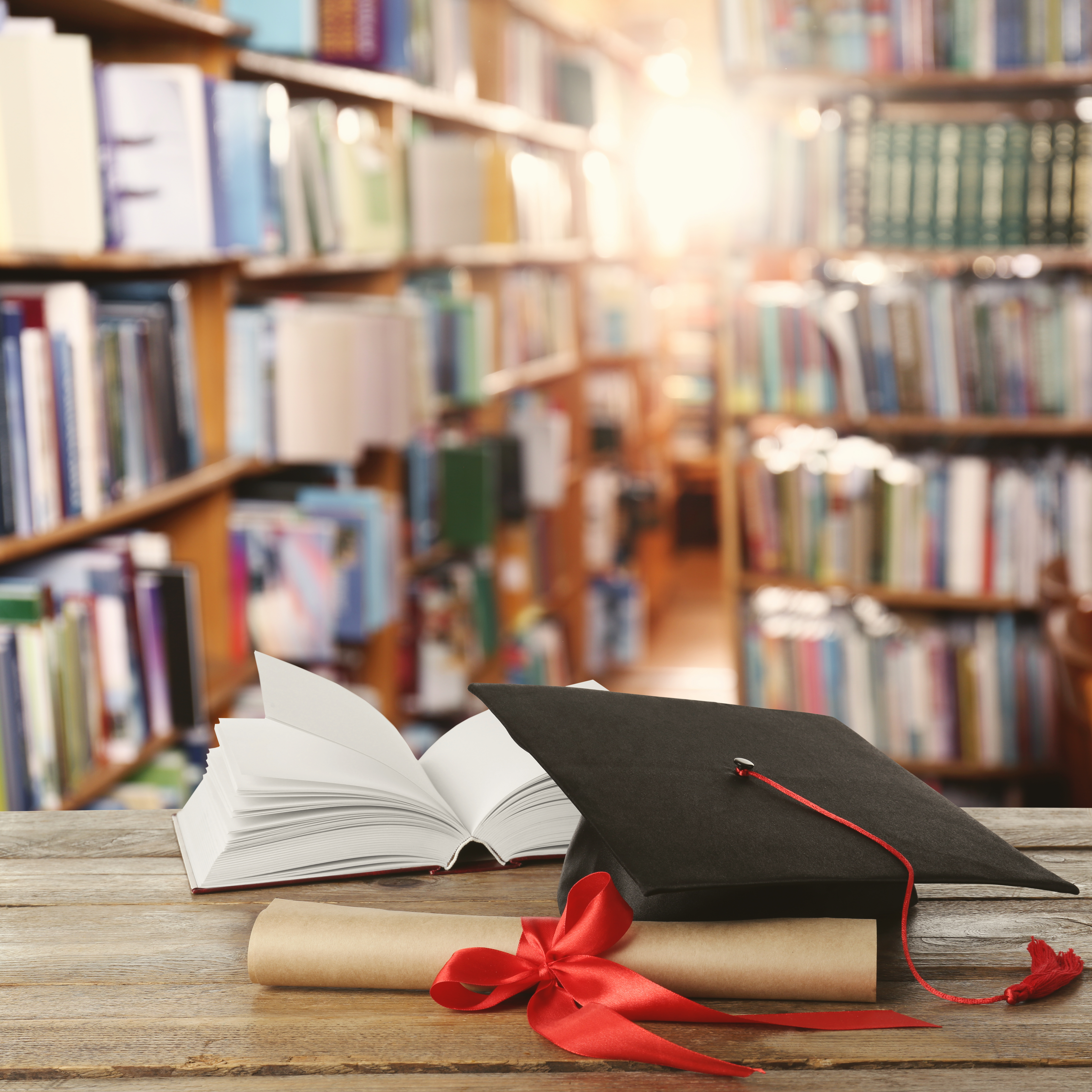Open book, grad cap, and diploma on a table in a library