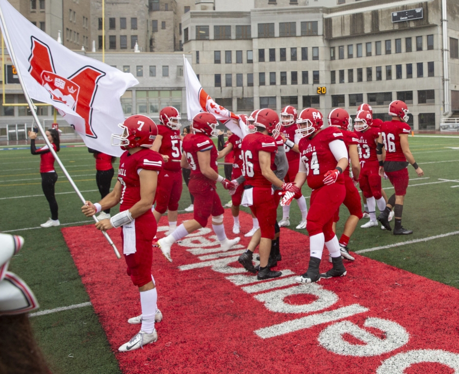 McGill Redbirds Warm Up the Crowd. Group of football players on the field with McGill flag.