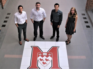 Four student award recipients stand around the McGill Athletics logo which is tiled on the floor of a hallway in Currie Gym