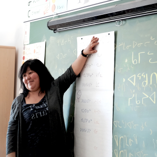 Inuit student teacher standing at a blackboard where she has written in Inuktitut