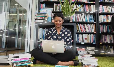 Student sitting on the library floor and using their laptop