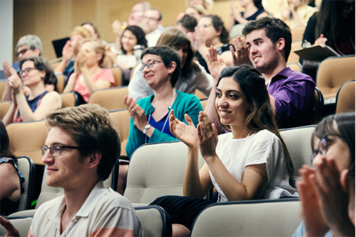 a group of people smiling and clapping in a lecture hall