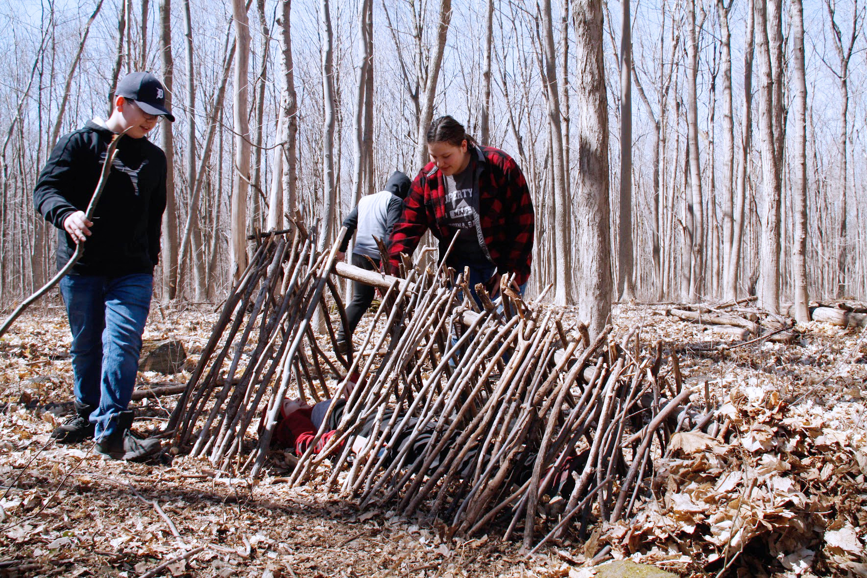 3 people building a shelter using woods and tree branches in a wood