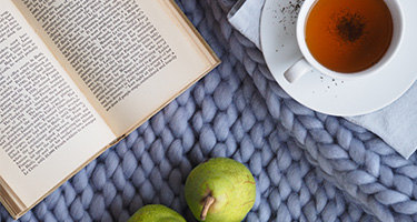 Top-view of an open book, a cup of tea, and fruits