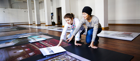 2 students organizing pieces of artworks on the floor in an empty hall