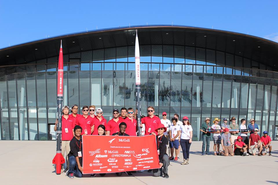 McGill Rocket Team posing for group photo while holding list of sponsors and rocket replicas in front of a building