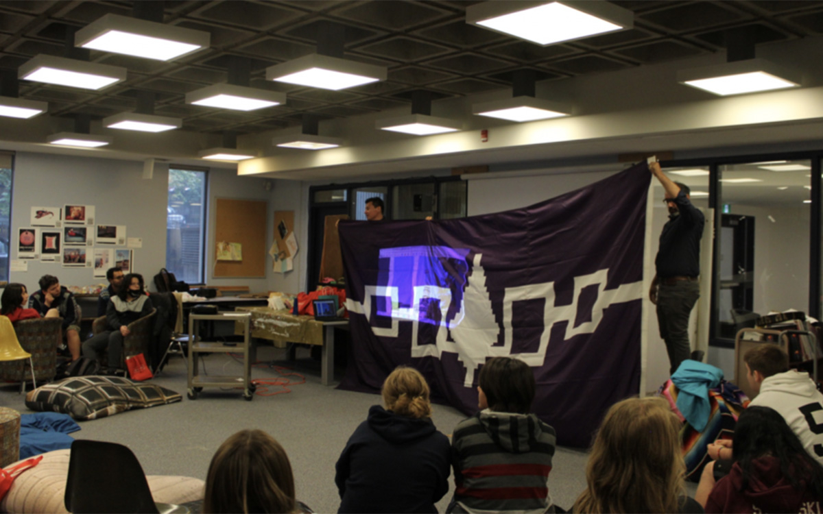 2 students holding the Hiawatha Wampum Belt Flag in front of a group of students