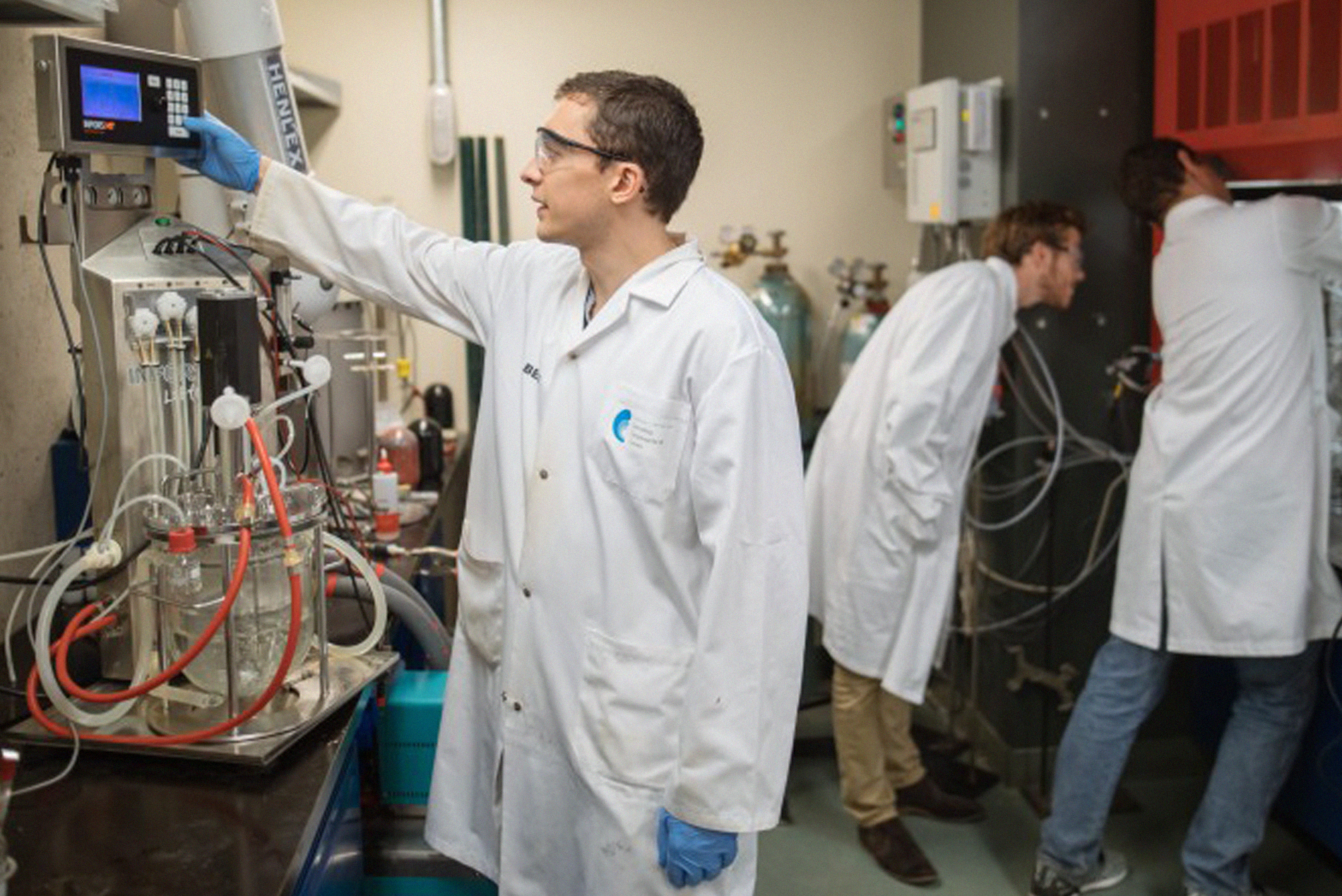 3 people working in a small laboratory with different equipment and wires