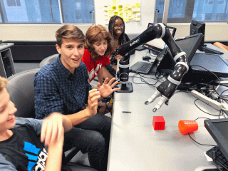 4 students talking and working with on a robotic arm