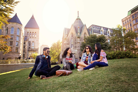 A group of students laughing while reclining on a grassy lawn