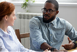 Headshot photos of a Black man talking with a White women with both siting at a desk