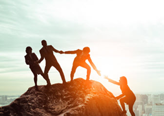 Image of the silhouettes of three people on top of a rock helping a fourth person reach the top