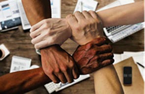 Overhead photo of four hands of various skin colours clasped together in a square