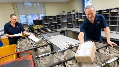 Deux hommes trient le courrier et les paquets dans de grands sacs postaux bruns.