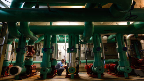 Espace intérieur avec de grands tuyaux en métal vert dans le cadre d'un système. Homme accroupi regardant les tuyaux au milieu de l'image.