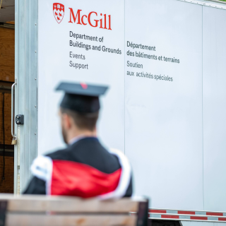 A truck from McGill's Buildings and Grounds with a decal of the university's logo. In the foreground, out of focus, someone wearing a convocation gown and cap.