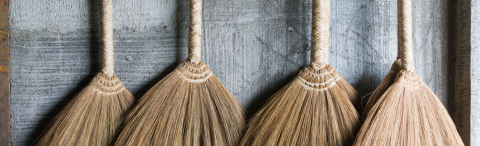 4 straw brooms attached to a concrete wall