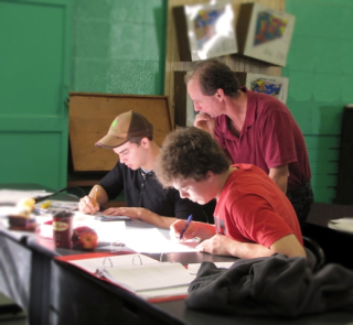 Students writing an exam under the watchful eye of an instructor.