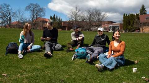 Five students lounge on the grass outside of the Macdonald-Stewart building