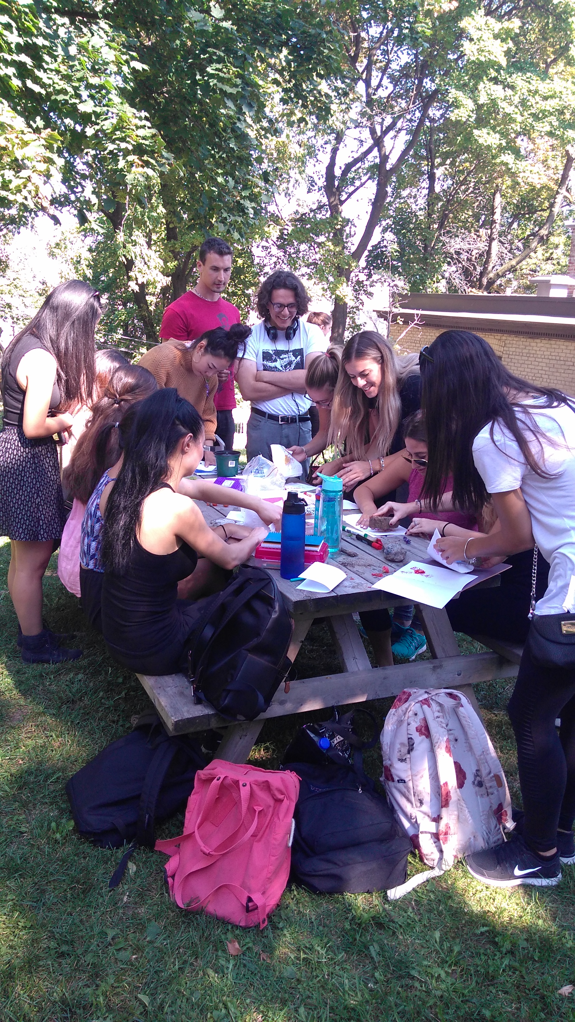 Students huddle around a picnic table covered in paper, flowers, rocks and hammers. 