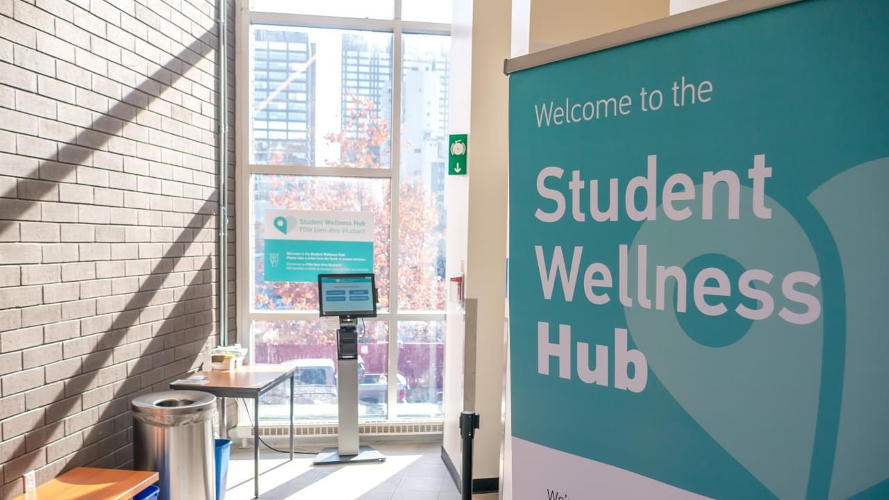 a standup banner reads Welcome to the Student Wellness Hub inside a sunny hallway