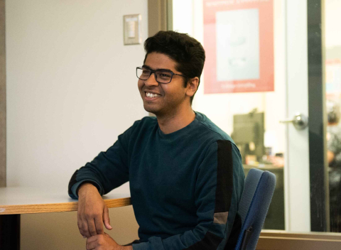 A smiling student seated at a desk in an advisor's office