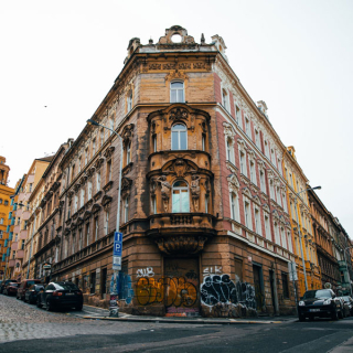 A large orange brick, graffiti covered building splits the urban stone road in Prague.