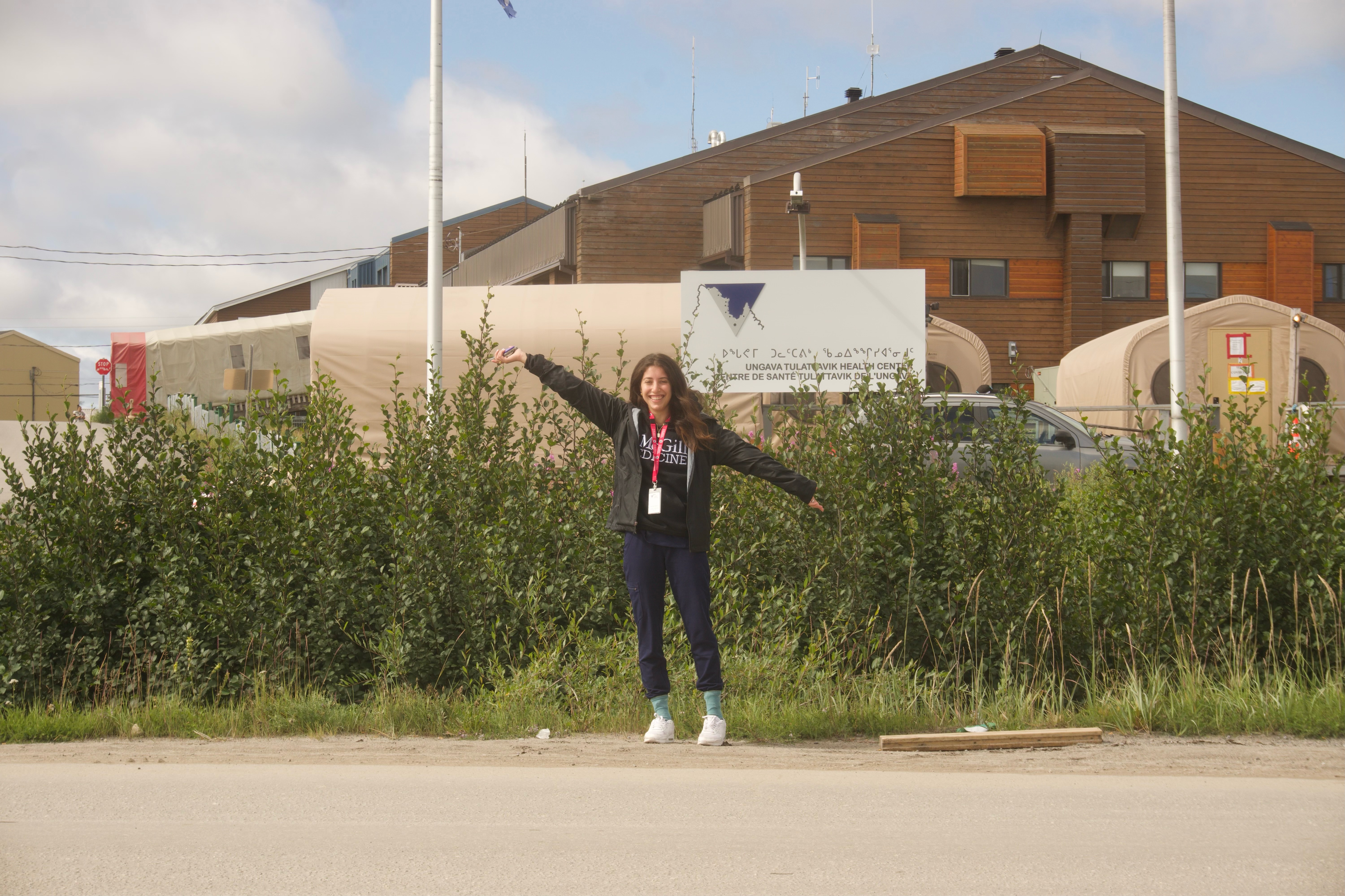 Lilly Groszman - young woman with brown hair posing outside her placement site wearinga McGill Medicine hoodie