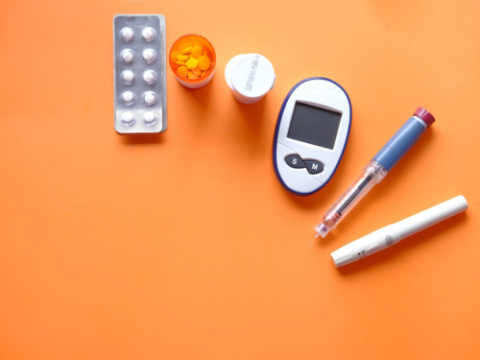 Pills in a blister pack, pills in a container, a glucometer, and insulin injection devices on an orange background