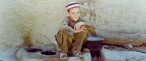 Young Afghan boy crouching and smiling at the photographer.