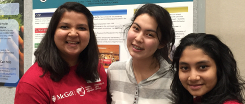 Three students pose in front of a poster