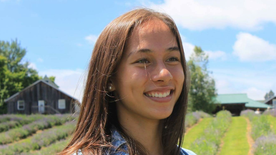 Allyson Kis - young woman with shoulder length brown hair wearing a denim jacket and standing in a field