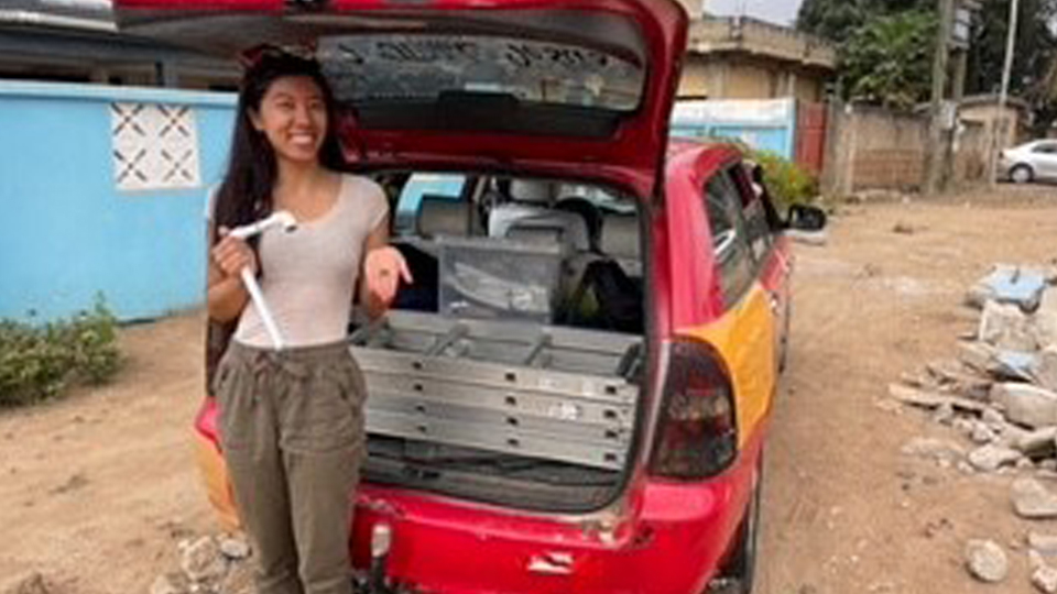 Maya Côté - young Asian woman holding tools and posing in front of an open car trunk full of research materials