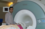 Dark hair man is standing next to the patient, half inserted in to MRI scanner