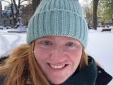 A young female student in a light blue winter hat is smiling in to the camera