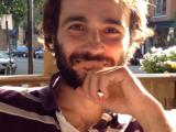 Sébastien Proulx, jeune homme barbu en chemise rayée, les cheveux baignés de soleil, souriant
