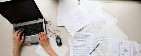 Thesis writing at a computer, surrounded by notes and research