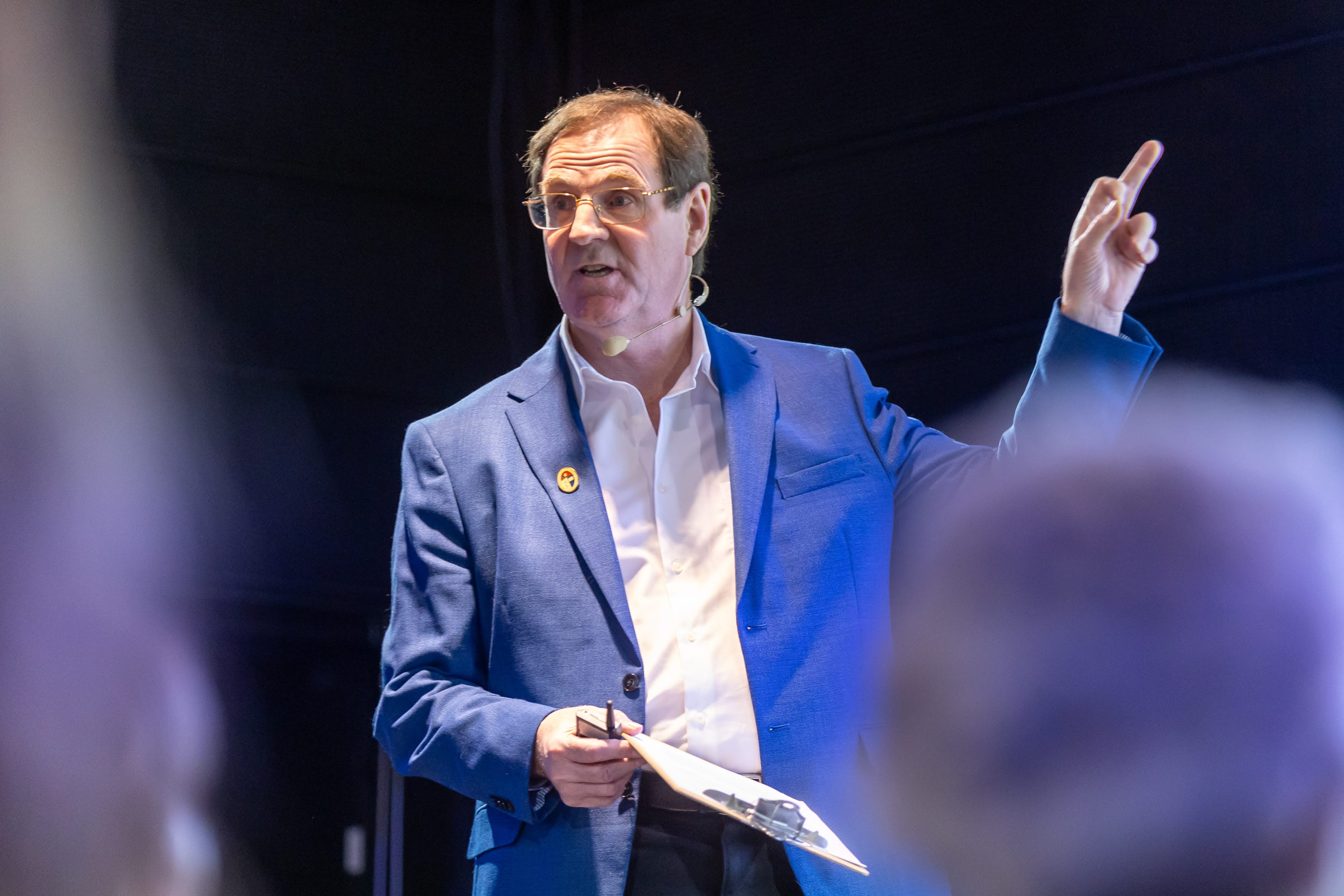 Alan Evans speaking on stage and pointing up