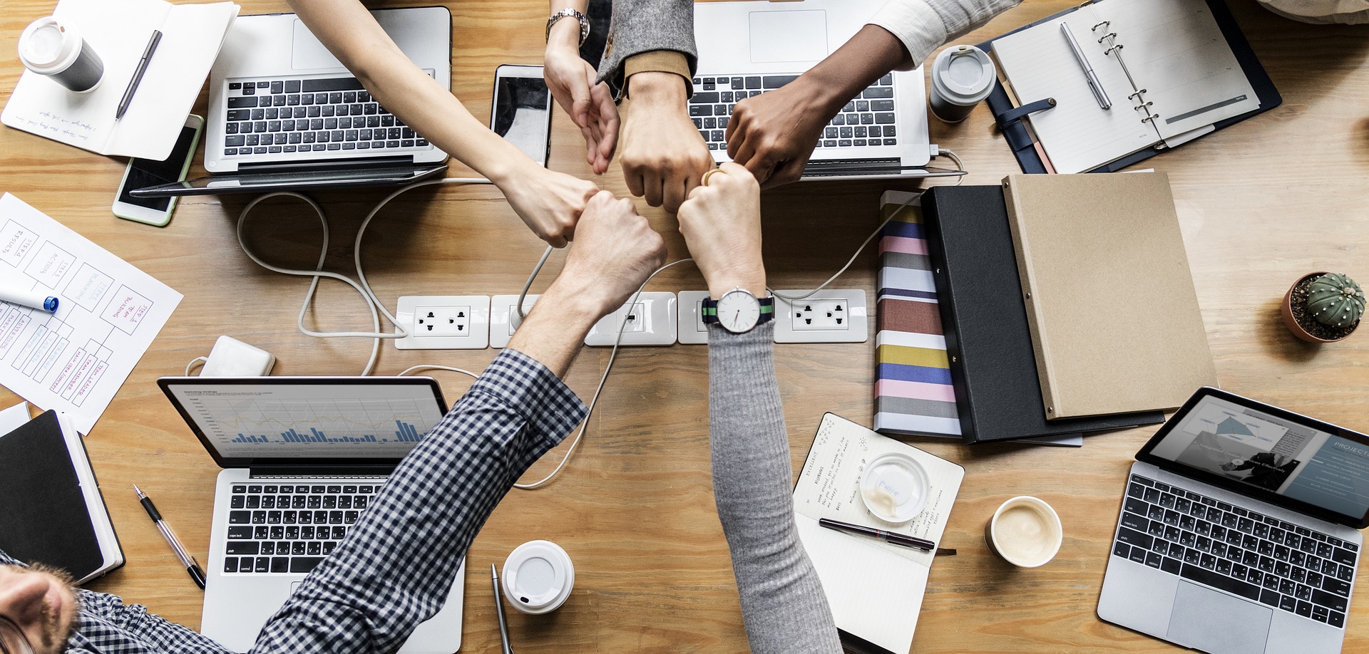 Group fist bump surrounded by computers and notebooks