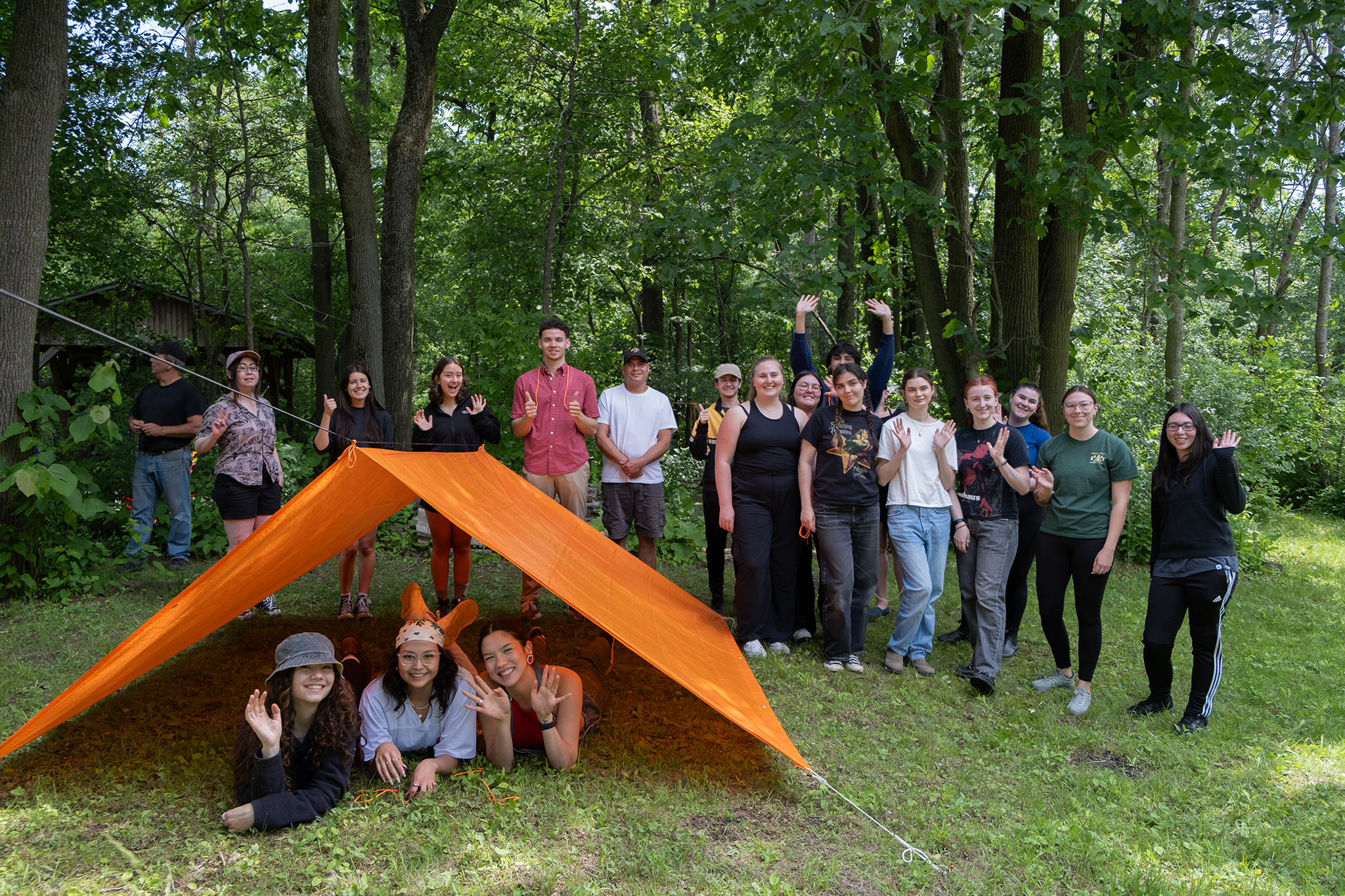 IMPRESS students at Wilderness Skills Training Day pose in the forest in front and under an orange tent 