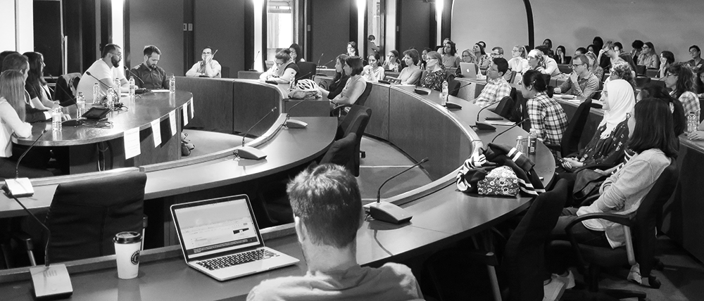 A large classroom filled with event attendees listening to a panel of speakers