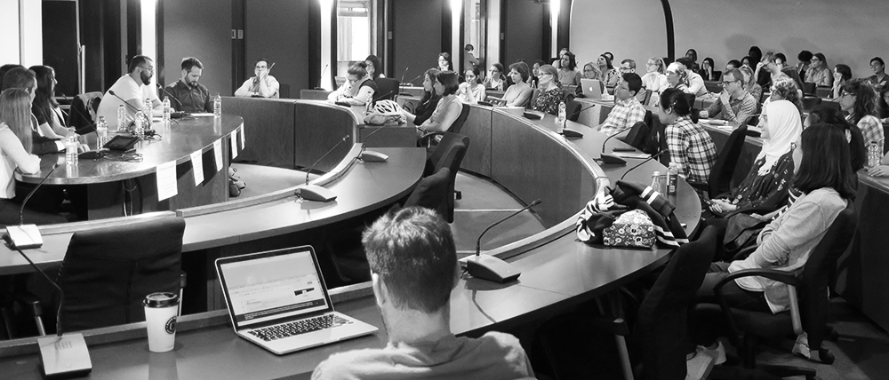 A large classroom filled with event attendees listening to a panel of speakers responding to a question