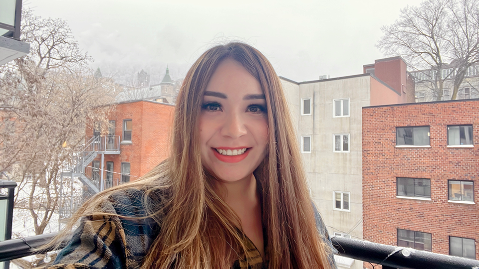 Picture of Cindy Garcia, a woman with long, blond-highlighted hair, parted in the middle, and brown eyes wearing a blue and beige plaid shirt set against a background of white and red brick buildings in winter.